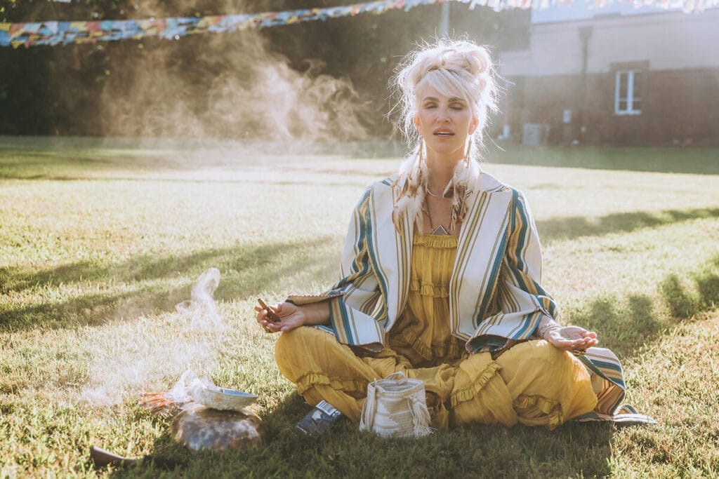 Woman meditating in sunlight with ceremonial smoke rising, preparing energetically and emotionally for a personal brand photoshoot