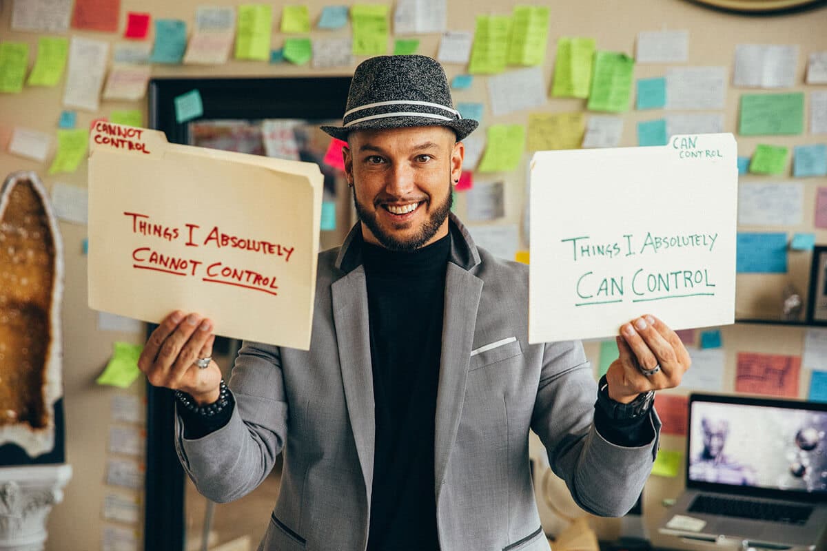 Jaramy Eugene Wilson smiling and holding two folders labeled “Things I Absolutely Can Control” and “Things I Absolutely Cannot Control” in a vibrant, post-it covered coaching space