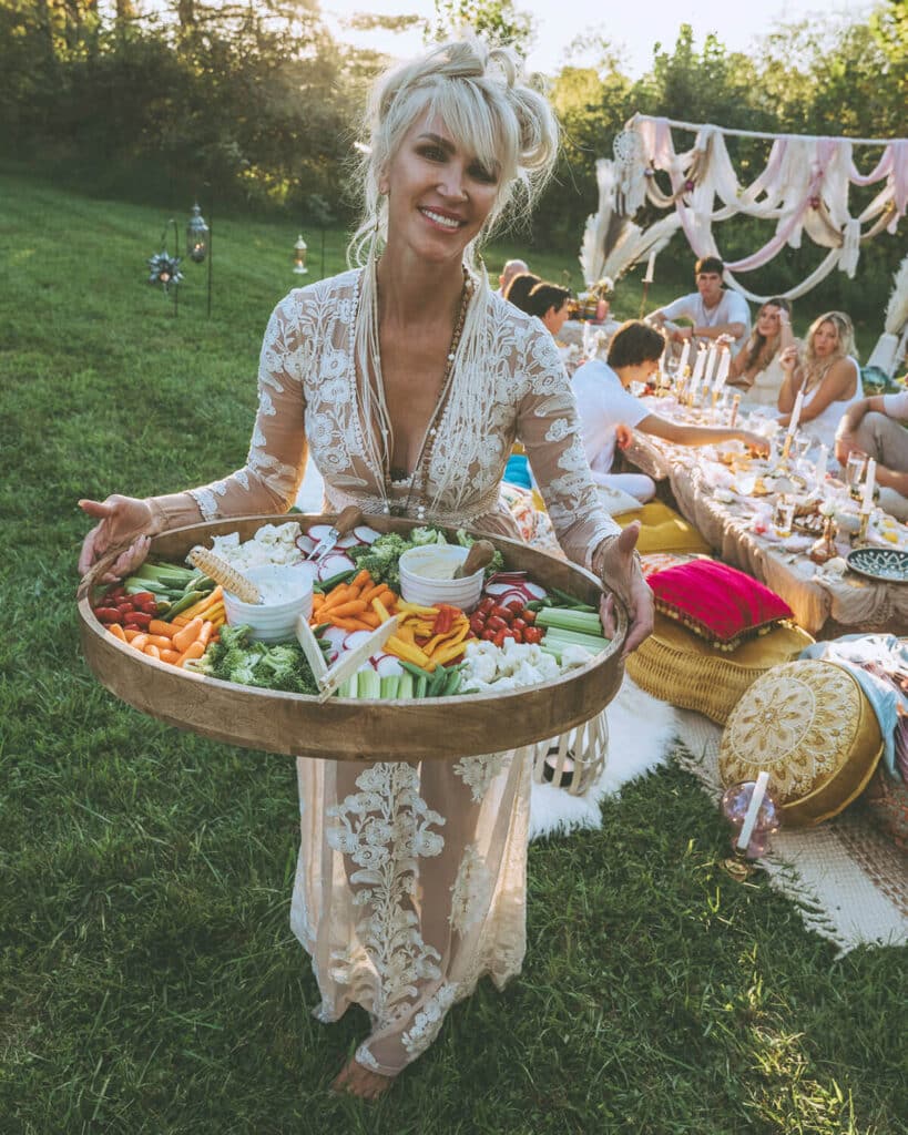 Woman holding a beautifully arranged platter of fresh vegetables at an outdoor gathering—showcasing lifestyle props that reflect community, nourishment, and intentional brand storytelling in a personal brand shoot