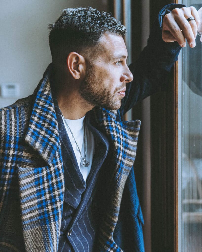 Client standing before a large window, natural light streaming in, reflecting on self-image before a personal brand shoot