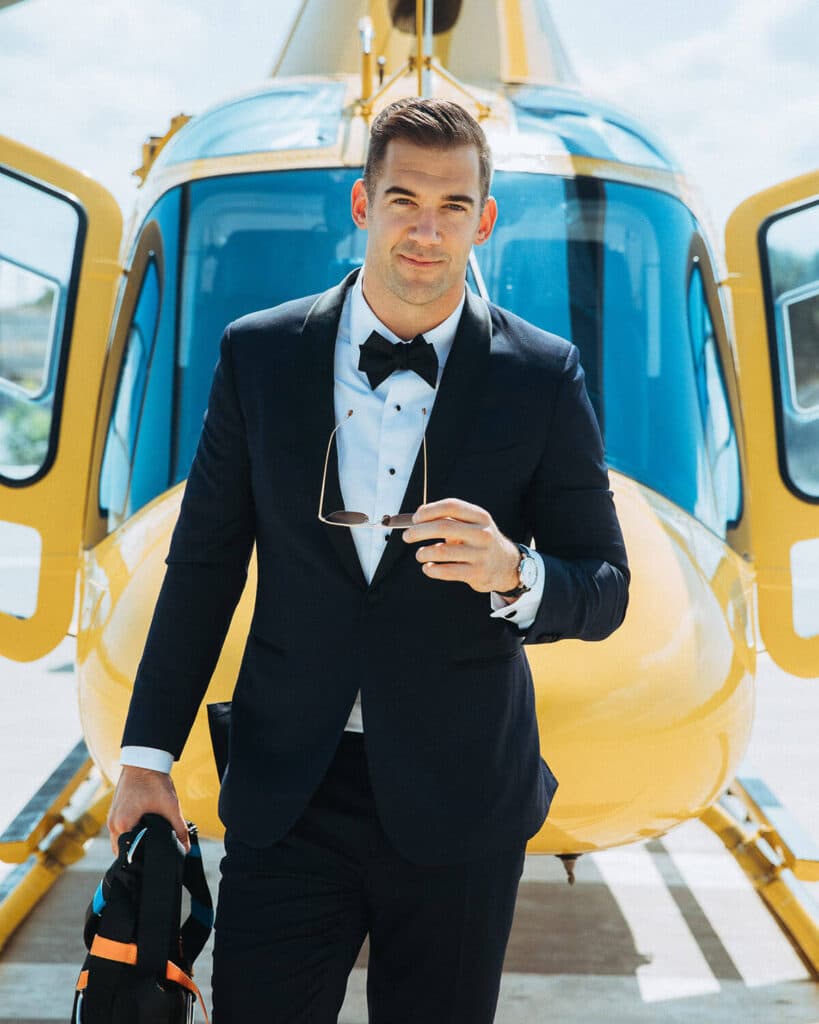 Lewis Howes in a tuxedo standing confidently in front of a helicopter — symbolizing high-level brand authority, luxury, and visual storytelling through Elevated Realism™