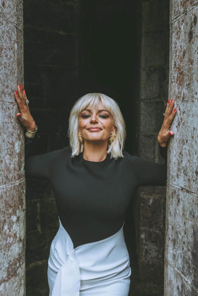 Caoimhe Harrison in divine feminine expression standing in the ancient stone corridor of a castle in Ireland