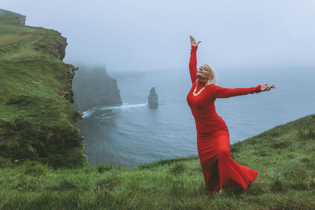 Editorial portrait of Caoimhe Harrison in flowing silk gown with arms open, channeling divine feminine power
