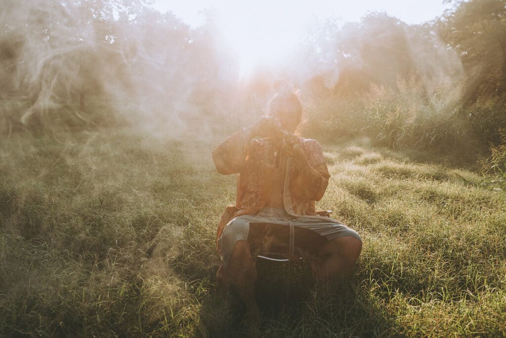 Nick Onken seated in a sunlit field, offering mapacho in sacred ritual, surrounded by smoke and light — symbolizing presence, intuition, and honoring the unseen