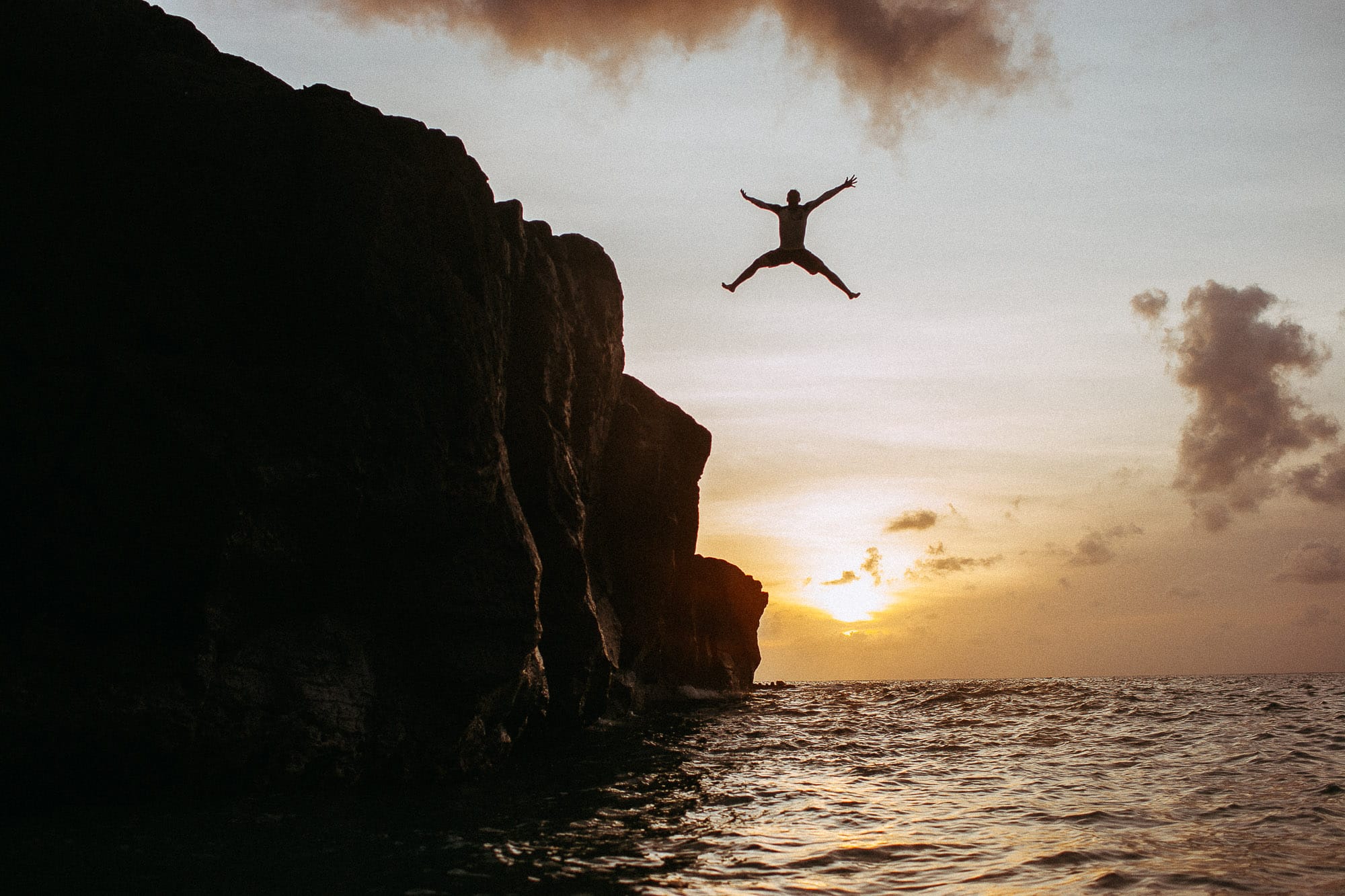 Silhouetted figure leaping from a sea cliff at sunset, committing to one coherent personal brand identity